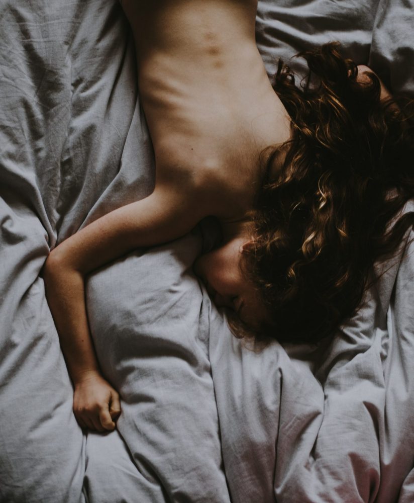 A naked girl laying in gray bedsheets